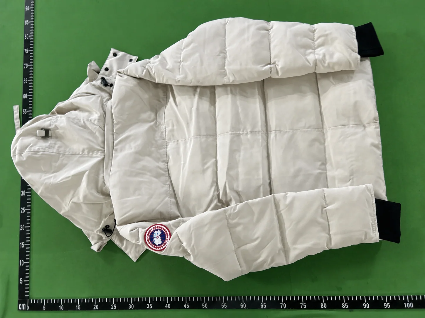 Rear QC view of an off-white fur-trim hood parka laid against a centimetre reference board